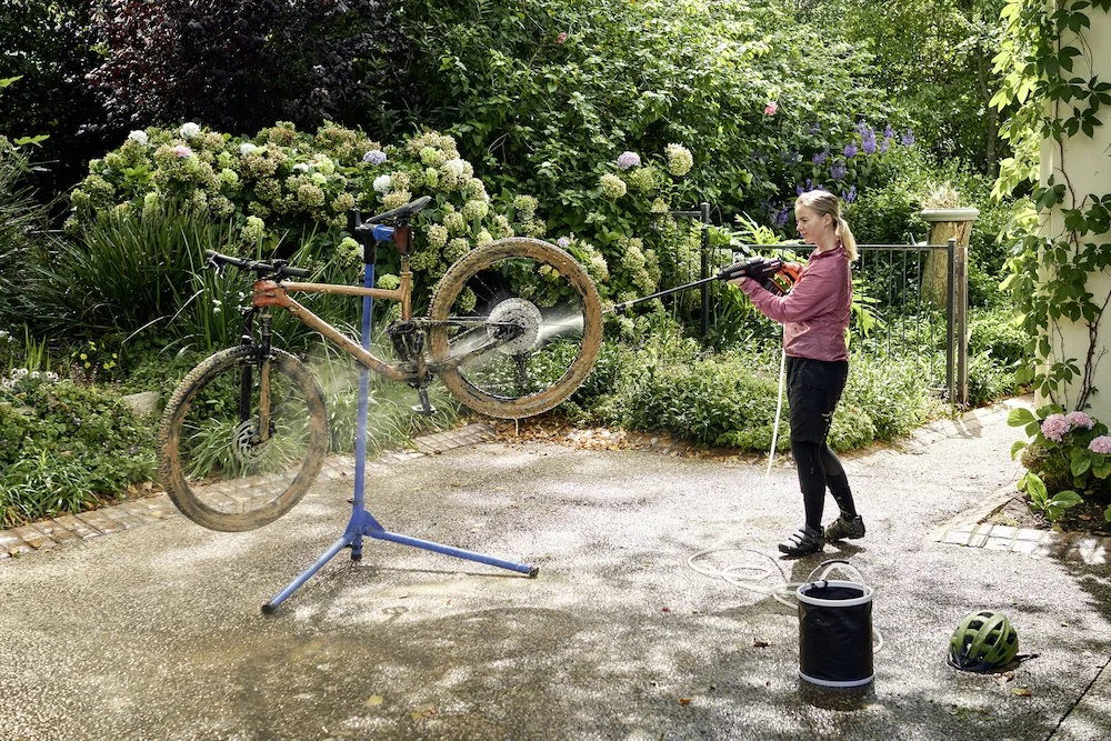 Person reinigt Fahrrad mit Hochdruckreiniger.